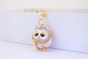 Close-up of golden owl keychain with white enamel, rhinestones and opal stone decoration