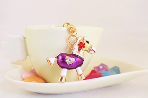 Détail d'un porte-clés poney en émail violet avec strass posé sur le bord d'une tasse