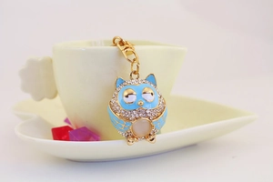 Close-up of golden owl keychain with blue enamel and white crystals on ceramic cup