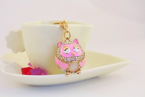 Detailed view of pink enamel owl keychain with sparkling rhinestones on coffee cup