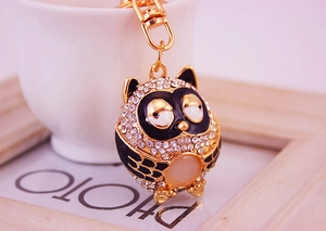 Detailed macro view of a gold owl keychain featuring rhinestones and a pink cat eye stone