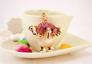 Detail of pink rhinestone elephant keychain with opal stone hanging on a white tea cup