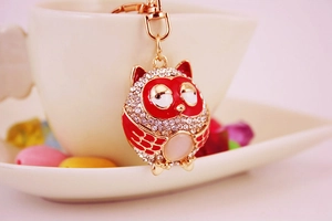 Close-up of red owl keychain with crystals hanging on a white ceramic mug rim