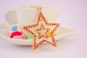 Detail showing the star pendant with orange-pink rhinestones on a gold-plated key chain