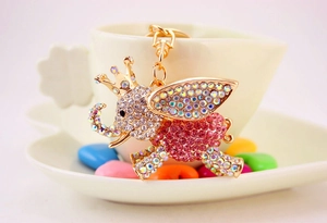Exquisite pink winged elephant keychain with rhinestones hanging on a coffee cup