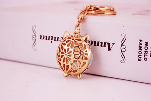 Detailed view of a gold hollow owl keychain hanging on a white decorative book edge