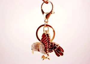Detail view of kingfisher keychain with red wings and crystal studs on a gold metal base