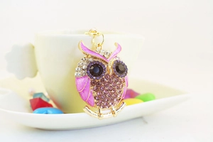 Close-up of a crystal-studded owl keychain with purple enamel on a white ceramic cup