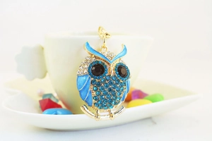 Detail of owl keychain with blue crystals and enamel on a white ceramic coffee cup