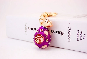 Detail of a purple rhinestone fortune bag keychain with golden lucky character and key ring