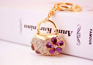Detail of a handbag-shaped keychain with purple floral gemstones and clear rhinestones