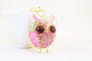 Detail of owl keychain with pink rhinestones and enamel wings by a white cup