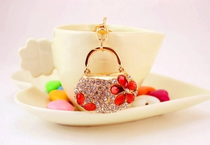 Detail of crystal handbag keychain with red heart flower on a beige coffee cup