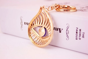 Detailed view of evil eye keychain with blue bead and gold plating next to a book