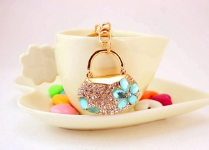 Close-up of golden rhinestone handbag keychain with blue crystal flowers on a tea cup