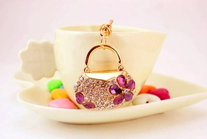 Detail of a handbag-shaped gold keychain with rhinestones and purple flower charms