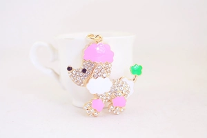 Nahaufnahme funkelnder Pudel-Schlüsselanhänger mit rosa Emaille-Ohren auf weißer Tasse