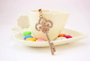 Vue détaillée du pendentif clé vintage en or serti de strass blancs sur le bord d'une tasse