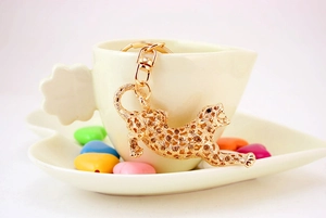 Detail of golden leopard keychain with amber rhinestones hanging on a white cup