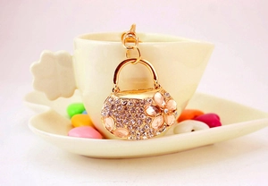 Detail of gold alloy handbag keychain with white and pink rhinestones on a coffee cup