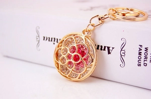 Close-up of golden rhinestone flower keychain with pink crystals on white book background