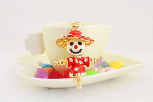 Detail of red enamel scarecrow keychain with crystals next to a white coffee cup