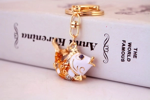 Detail of a golden fish keychain with white enamel, rhinestones and purple eye crystal