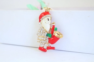 Detailed macro of Santa Claus brooch with crystals playing saxophone on white surface