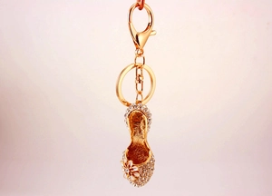 Detailed view of rhinestone encrusted gold high heel keychain with white flower petal