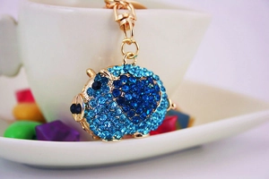 Detail of blue rhinestone pig keychain with golden alloy lobster clasp on white cup
