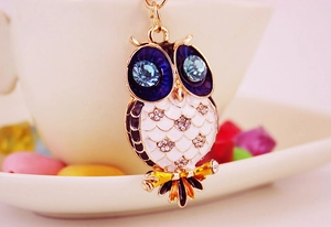 Macro shot of owl charm with blue rhinestone eyes and enamel details on gold alloy base