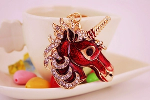 Close-up of red unicorn keychain with gold metal frame and white rhinestones detail