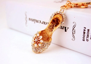 Detail of gold high heel keychain with white rhinestones and a daisy flower on a book