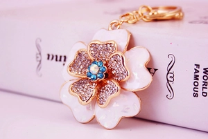 Macro detail of alloy flower keychain with white enamel petals and blue rhinestone center