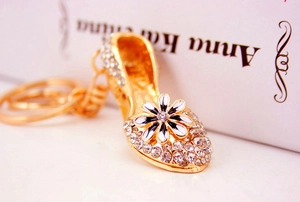 Detailed close-up of golden high heel keychain with white rhinestones and daisy flower