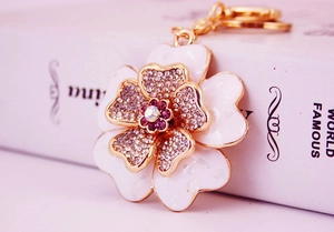 Close-up of golden floral keychain with white enamel petals and purple crystal center