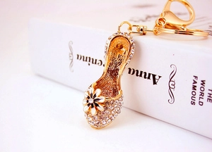 Detailed close-up of golden rhinestone high heel keychain with black enamel daisy flower