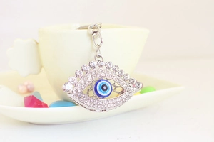 Détail d'un porte-clés œil grec en argent serti de strass blancs sur une tasse
