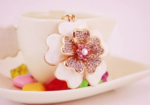 Close-up of white enamel flower charm with sparkling crystal core on a gold metal frame