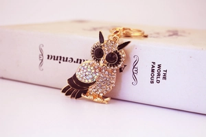 Vue détaillée porte-clés hibou doré avec strass scintillants sur bord de livre blanc