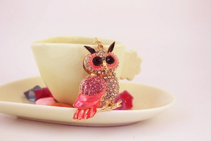 Close-up of owl keychain with pink rhinestones and enamel resting on a yellow coffee cup