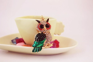 Detailed view of crystal-studded owl pendant with green enamel wings and red eye accents