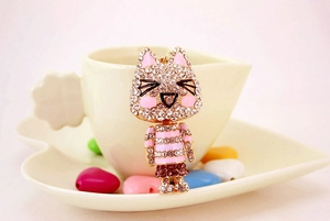 Detail of cute rhinestone cat keychain resting on a white coffee cup with pink accents