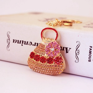Goldener Handtaschen-Schlüsselanhänger mit roten und rosa Kristallen vor weißem Buch