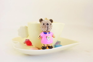 Détail d'un porte-clés ours avec robe en émail rose et strass sur une tasse à café