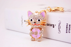 Close-up of sparkling crystal-encrusted lucky cat keychain with golden finish and purple accents