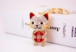 Close-up of golden lucky cat keychain with white rhinestones and engraved red coin charm
