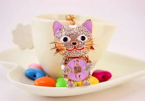 Detailed view of lucky cat keychain with white crystals and purple enamel on a gold base