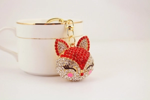 Detail of fox-shaped keychain with red and clear rhinestones hanging on a white porcelain cup