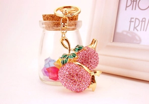 Dettaglio del portachiavi a forma di pesca con strass rosa e finitura dorata lucida
